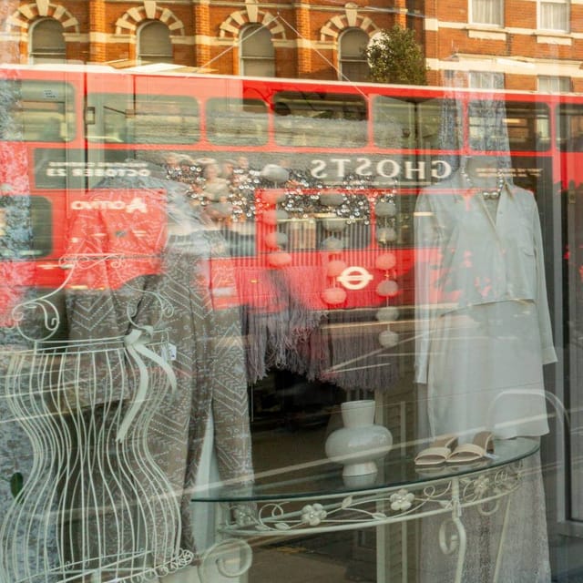 A shop window reflecting a red-brick terrace and a passing red bus over the mannequins inside